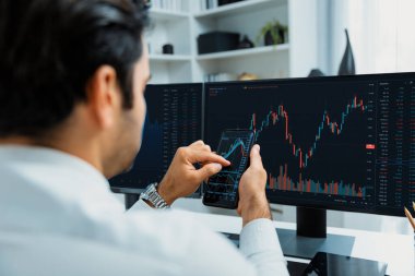 Akıllı telefondan akıllı telefon arayan tüccar işadamı, bilgisayardaki dinamik borsa yatırım ekranını analiz ediyor ve modern merkez ofisteki en kârlı finansal teknoloji pazarına yatırım yapıyor. Tahmin et..