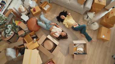 Oturma odasında yere uzanmış, mobilyaları etrafa saçılmış kız arkadaşın yukarıdan görünüşü. Lezbiyen aşıklar konuşurken tavana işaret ediyorlar. Myrmidon.