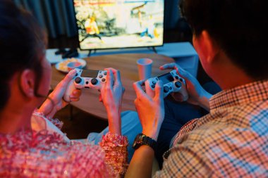 Joystickli çiftler arka tarafta oturup video oyunu oynuyorlar. Önden atıştırmalıklar ve modern evdeki neon ışıklı oturma odasında eğlenceli ruh halleri olan içecekler. İnfobahn.