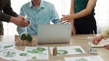 Yel değirmeni modeline ve ev şeklindeki bloğa danışmanlık yapan işadamları, Dünya Yöneticisi 'nin dizüstü bilgisayar üzerinde çalışmasını kurtarmak için yeşil enerji kullanımına referans olarak başvuruyorlar. Tanımlama.