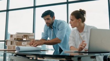 Akıllı mühendis proje planını kullanarak genç iş arkadaşına ev modeli inşaatını açıklıyor. Profesyonel mimar masadaki proje planına mimari model ve planla işaret ediyor. İzleme