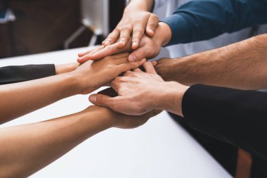 Çeşitli ofis çalışanlarından oluşan bir grup, ofis odasında el ele vererek iş sinerjisini ve iş yerindeki güçlü verimli takım çalışmasını sembolize ediyor. İş çalışanları arasındaki işbirliği ve birlik. Tedbirli