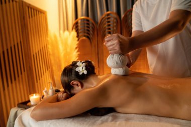 Sıcak bitkisel top spa masaj vücut tedavisi, masör kadın vücuduna nazikçe şifalı bitki torbası bastırıyor. Aromaterapi tesisinin sakinliği ve dinginliği kaplıca salonundaki mumların sıcacık ışığında. Sessiz.