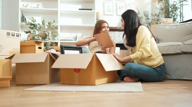 Kutudan kitap seçen ve oturma odasında kitap okuyan mutlu lezbiyen çift. Taşınırken kutular ve mobilyalarla çevrili otururken çekici bir kız konuşuyor ve paketleri açıyor. Yer değiştirin. Myrmidon.