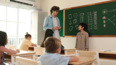 Öğrenci sınıfın önünde duruyor ve beyaz bir öğretmen öğrenciye bakıp çocuğu cesaretlendirirken kendini sınıfa tanıtmaya başlıyor. Çeşitli çocuklar oturur ve oğlanlara bakarlar. Pedagoji.