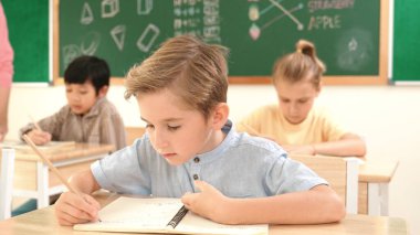 Çekici beyaz çocuk okulda matematik okurken kameraya bakıyor. Çeşitli şirin öğrenciler test yaparken öğretmen Asyalı çocuklara soru sorup tahtaya kağıt doğrultuyor. Pedagoji.
