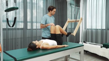 Pilates hocası, Cadillac teçhizatı üzerindeki bacak kaldırma egzersizi sırasında bir müşteriye yardım ediyor. Öğrenci uzanıyor ve temel dayanıklılık ve bacak esnekliğini arttırmak için Cadillac 'ın üzerinde bacak daire çiziyor. Alışkanlık.