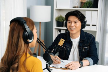 Gülümseyen radyo etkili sunucusu kulaklık takıyor kadın konuşmacı ile röportaj yapıyor sosyal medya internet sitesinden dinleyicilere bilgi paylaşıyor stüdyo kaydında sabah canlı yayın kanalı. İnfobahn.