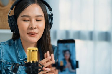 Asyalı sunucu canlı yayında canlı yayında canlı yayında sosyal medyada kulaklık takarak konuşuyor. Dinleyicileri modern stüdyoda koçluk yaparak selamlıyor. Taktik.