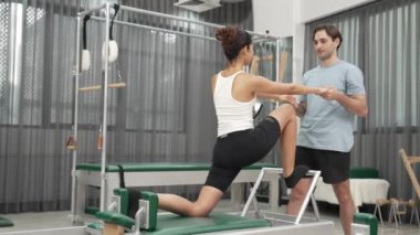 Esneklik ve çekirdek eğitimi için pilates kursunda trapez masasında destek alan bir kadın. Öğrenci dengeyi geliştirmek için reformcuları iki büklüm ediyor. Alışkanlık.