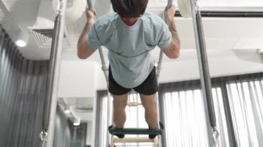 Çekirdek dayanıklılığı ve spor salonunda vücut egzersizi için pilates trapez masasına tırmanan bir adam. Eğitmen, arka ve kalça esnekliğini arttırmak için Cadillac 'ta ters asılı duruyor. Alışkanlık.