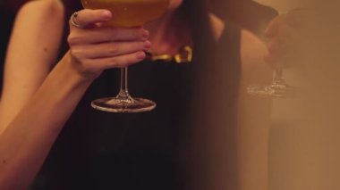 Kapanışta güzel bir kadın, gece kulübü tezgahı partisinde gece yarısı sıcak ışıklarıyla hindistancevizli, köpüklü içeceğe cam karıştırılmış meyve suyu kokteyli hazırlıyor. Vinosity.