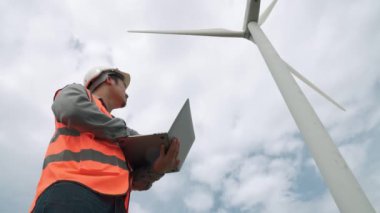 Gökyüzü arka planına sahip bir rüzgar türbini üzerinde çalışan mühendis. Yenilenebilir ve sürdürülebilir enerjinin gelecekteki üretimi için yenilikçi bir ideal. Rüzgar türbininden enerji üretimi.