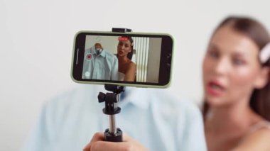 Genç sosyal medyum kadın moda videosu yapıyor. Blogcu kameraya selfie çubuğu ve ışık halkası kullanarak gülümserken, aynı zamanda ikna edici çevrimiçi kıyafetlerin izleyicilere veya takipçilere vlog satmasını sağlıyor. Düzenle