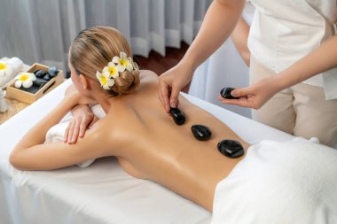 Lüks tatil köyündeki kaplıcalarda sıcak taş masajı. Gün ışığı sükunet ortamında, mutlu kadın müşteri bazalt taş masajından zevk alıyor. Rahatlatıcı bir sıcaklıkla vücudun üzerinde süzülüyor. Sessiz.