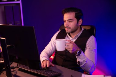 Gülümseyen zeki işadamı, elinde kahve fincanı olan satış ekibiyle buluşuyor ve geceleri Mor Neon Light Home Office 'deki bilgisayar ekranında ürün hedef pazarını araştırıyor. Tahmin et..