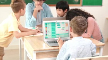 Zeki beyaz çocuk STEM teknoloji sınıfında farklı öğrenci ve öğretmenlerden oluşan bir grup zihin haritalama yaparken dönüp kameraya bakıyor. Akıllı çocuk kodlama yazılımı öğreniyor. Pedagoji.