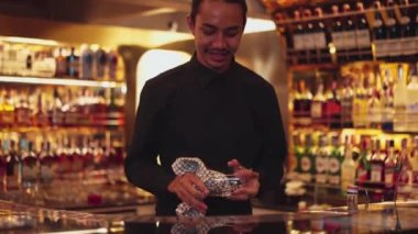 İyi görünümlü, gülümseyen Asyalı, zeki barmen, lüks içki tezgahı sahnesinde bardakları siliyor. Profesyonel barmen kostümü içinde, gece kulübü konforuna sıcak bakıyor. Vinosity.