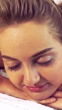 Rahatlamış genç bir kadın masaj için spa yatağında uzanıyor. Lüks bir spa merkezinde masaj terapistinin geleneksel otlarını ve baharatlarını kullanıyor. Sağlık, stres atma ve gençleştirme kavramı.