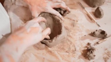 Kızların el modelliği masasında ekipman olan bir fincan kilin üst görüntüsü. Liseli kız çömlekçilik sınıfında kil oynuyor ya da şekillendiriyor. El işçiliğine ve el yapımı cam yapımına yakın çekim. Öğretim