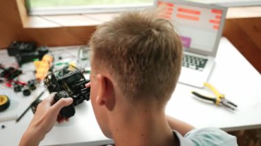 Elektronik ekipman ve dizüstü bilgisayar görüntüleme programı olan mutlu öğrenci çalışma arabası modeli inşaatının üst görüntüsü STEM sınıfında dağılıyor. Yaratıcı eğitim. Öğretim