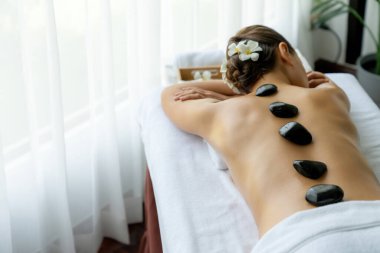 Lüks tatil köyündeki kaplıcalarda sıcak taş masajı. Gün ışığı sükunet ortamında, mutlu kadın müşteri bazalt taş masajından zevk alıyor. Rahatlatıcı bir sıcaklıkla vücudun üzerinde süzülüyor. Sessiz.