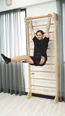 Asılı bacak egzersizi yapan mutlu bir adam vücut kaslarını güçlendirmek ve beden eğitimini iyileştirmek için duvar parmaklıkları üzerinde egzersiz yapıyor. Alt karın bölgesini iyileştirmek için erkek antrenör bacak yükseltme ameliyatı. Alışkanlık.