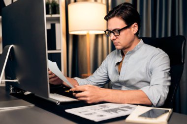 Akıllı iş adamı iş paragrafı dinamik pazarlama analizi planını analiz ediyor. Kağıt kağıtları ve bilgisayar monitörü raporlarını gece evdeki belge verileriyle karşılaştırmak için hazırlıyor. Bireysel.