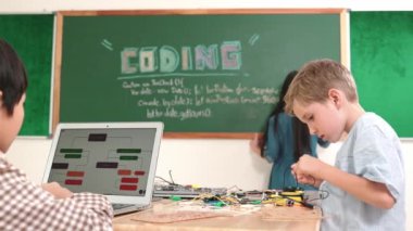 Kafkas arkadaşı STEM sınıfında elektrik panosunu tamir ederken Asyalı çocuk kodlama programı. Enerjik öğrenci kodlama mühendisliği komut yazarken ve yapay zeka yazılımını programlarken tahtada duruyor. Pedagoji.