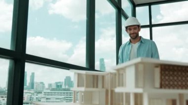 Gökdelen manzarasına bakarken yürüyen profesyonel mimar mühendisi. Masaya yerleştirilmiş ev modeliyle pencereye bakarken yetenekli proje yöneticisi proje planını tutuyor. Tasarım. İzleme