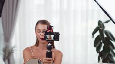 Sosyal medya için güzellik ve kozmetik video içeriği hazırlayan genç bir kadın. Güzellik blogcusu kameraya gülümserken seyircilere ve takipçilere güzellik bakımını gösteriyor. Düzenle