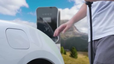 İlerici adam şarj noktasında elektrikli araba yüklüyor, daha temiz bir çevre için temiz ve yenilenebilir enerjiyle çalışan bir EV ile doğada ve dağlarda seyahat ediyor..