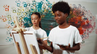 Çeşitli mutlu çocuklar renkli duvarlarla tuval boyarlar. Beyaz gömlek giyerek resim dersinde resim çizen çok kültürlü bir öğrenci. Yaratıcı aktivite konsepti. Öğretim.