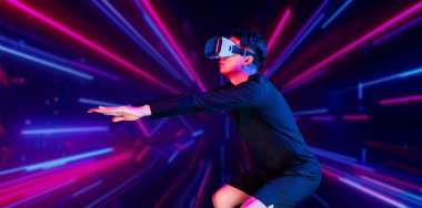 Asian man wearing VR headset while exercising at an abstract background with glowing pink and blue color. Attractive male model playing fitness while wearing black bodysuit. Technology. Ingenuity. clipart