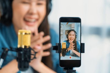 Asyalı sunucu canlı yayında canlı yayında canlı yayında sosyal medyada kulaklık takarak konuşuyor. Dinleyicileri modern stüdyoda koçluk yaparak selamlıyor. Taktik.