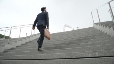 Akıllı bir iş adamının elinde çantayla merdivenlerden yukarı çıkışının en üst görüntüsü. Profesyonel proje yöneticisi merdivenlerden çıkıp işyerine gidiyor. Yeteneklerini arttırmak, terfi almak, seyahat etmek. Sevinçli..