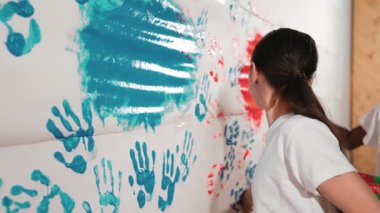 Küçük çocukların el kaplamalarını renkli ve boyalı duvarlarla çiziyorlar. Sanat dersinde kırmızı ve maviyle boyanmış boya odasıyla karışık ırk tutma tepsisiyle lise öğrencisi. Yaratıcı aktivite. Öğretim