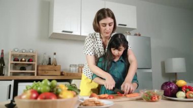 Zeki beyaz anne ve Asyalı kız birlikte yemek pişiriyor ve sebze doğruyor ya da akşam yemeği için salata hazırlıyor. Mutlu anne ve kız taze yemekle sağlıklı yemek yapıyorlar. Sağlıklı gıda konsepti. Pedagoji.