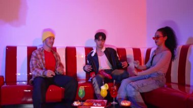 Bir grup break dansçı restoranda oturuyor ve pembe neon ışıklı müzik eşliğinde hareket ediyorlar. Profesyonel hipster dans ediyor ve birlikte otururken enerjik bir hareket sergiliyor. Mutluluk.