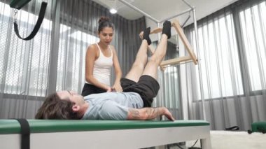 Cadillac ekipmanları üzerinde bacak kaldırma egzersizinde müşteriye yardımcı olan yetenekli pilates eğitmeni. Kadın antrenör, Cadillac 'ın bacak gerdirme hareketine yardım ediyor. Temel bağlantıyı geliştirmek için, bacak esnekliği için. Alışkanlık.