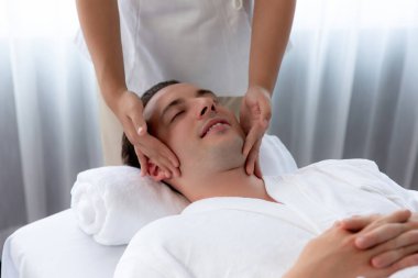 Beyaz adam stres önleyici kafa masajından ve lüks bir tatil beldesi veya otel spa salonundaki modern ışık ortamında yüz güzelliği eğlencelerini şımartmaktan hoşlanıyor. Sessiz.