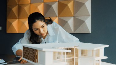 Ev modeli uzunluğunu ölçen Asyalı kadın mimar mühendisinin yakın çekimi. Genç, güzel proje yöneticisi ev modeli üzerinde çalışırken ev inşaatını kontrol ediyor. Yaratıcı tasarım konsepti. Yönlendirici.