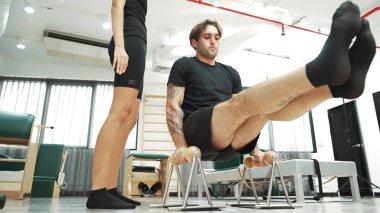 Müşteri, spor salonunda çekirdek dayanıklılığını, bacak dengesini ve kontrolü artırmak için pilates seansı sırasında eğitmen rehberliği ile oturarak bacak kaldırma alıştırması yapıyor. Pilates yapan mutlu adam. Alışkanlık.
