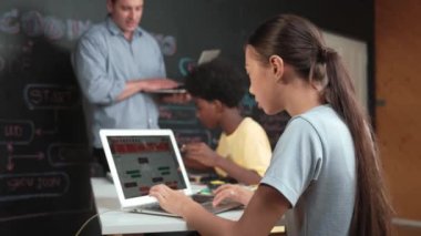 Afrikalı erkek manken tamir ederken beyaz kız programlama ya da kodlama sistemi. Öğretmen elinde dizüstü bilgisayar tutarken çeşitli çocukların web geliştirme programı yazmalarına bakıyor. Yenilik eğitimi. Öğretim