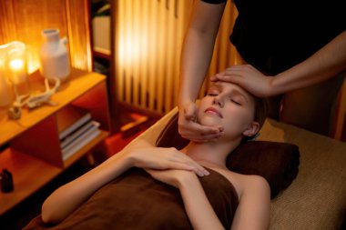 Beyaz kadın stres önleyici kafa masajı yapmaktan ve lüks otel veya otelde sıcak mum ışığında yüz güzelliği eğlencesi yapmaktan zevk alıyor. Sessiz.