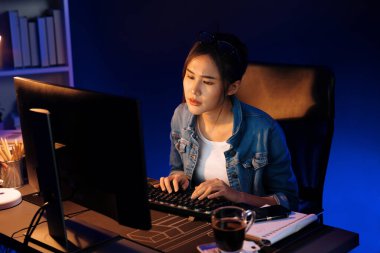 Stresli, genç, güzel Asyalı yaratıcı proje yaratıcısı sosyal medyayı araştırmak için bilgisayara bakıyor ve geceleri daha çok neon modern ofisin planlama kanalı stratejisine ulaşılıyor. Taktik.