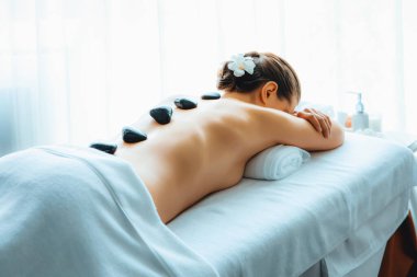 Lüks tatil köyündeki kaplıcalarda sıcak taş masajı. Gün ışığı sükunet ortamında, mutlu kadın müşteri bazalt taş masajından zevk alıyor. Rahatlatıcı bir sıcaklıkla vücudun üzerinde süzülüyor. Sessiz.