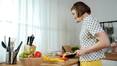 Enerjik anne, mutfak malzemeleri ile çevrili sebzeleri doğrarken modern mutfakta kahvaltı için salata yapıyor. Akıllı kadın temizlikçi yemek pişirir ve yemek hazırlar. Sağlıklı bir yaşam tarzı. Pedagoji.