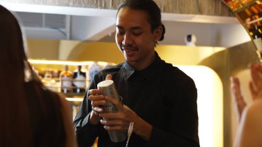 Asyalı akıllı barmen karışık kokteyl hazırlama sunumunu sallayarak lüks bir barın önünde güzel bir bayana özel bir içecek hazırlıyor gece hayatı lüksüyle. Vinosity.