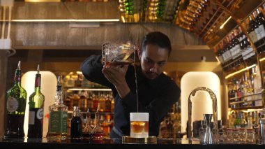 Asyalı barmen soğuk bardağa karışık viski dökerek soğutmalı buzlu içecek üretiyor. Lüks ılık barlarda alkol yenileme gösterisine odaklanan yaratıcı bir reklam yapıyor. Vinosity.